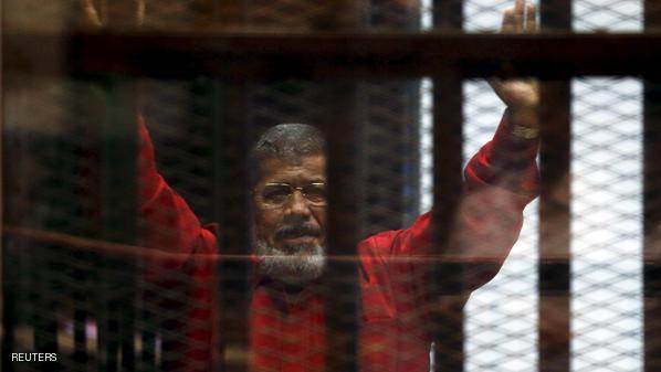 Deposed President Mohamed Mursi greets his lawyers and people from behind bars at a court wearing the red uniform of a prisoner sentenced to death,   during his court appearance with Muslim Brotherhood members on the outskirts of Cairo,   Egypt