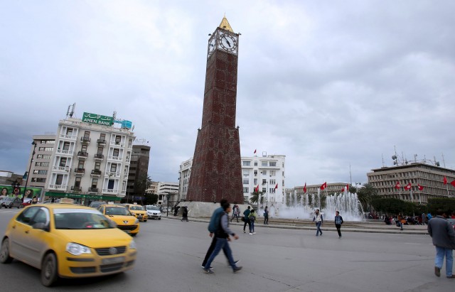 Cars and people pass by the clock tower at the end of Avenue Habib Bourguiba in Tunis
