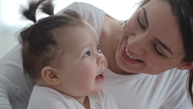 Mom kissing her little daughter while she laughing and clapping hands