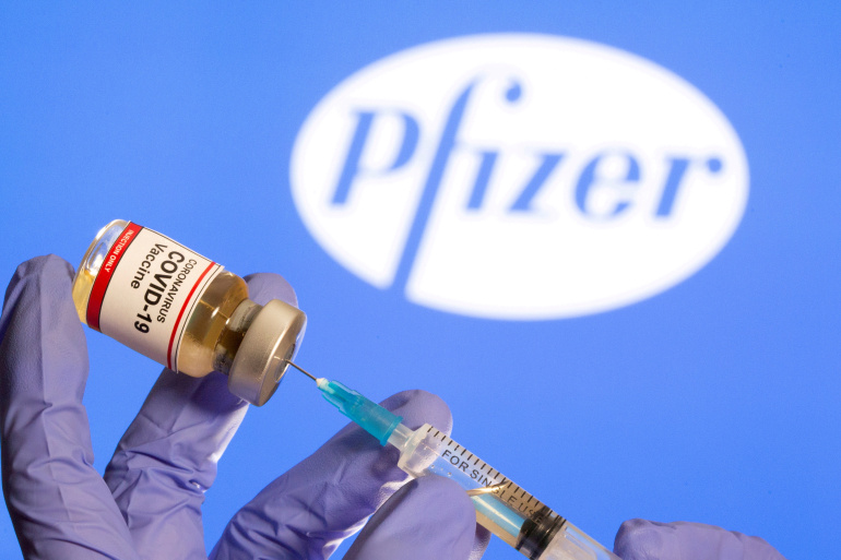 FILE PHOTO: A woman holds a small bottle labeled with a 'Coronavirus COVID-19 Vaccine' sticker and a medical syringe in front of displayed Pfizer logo in this illustration