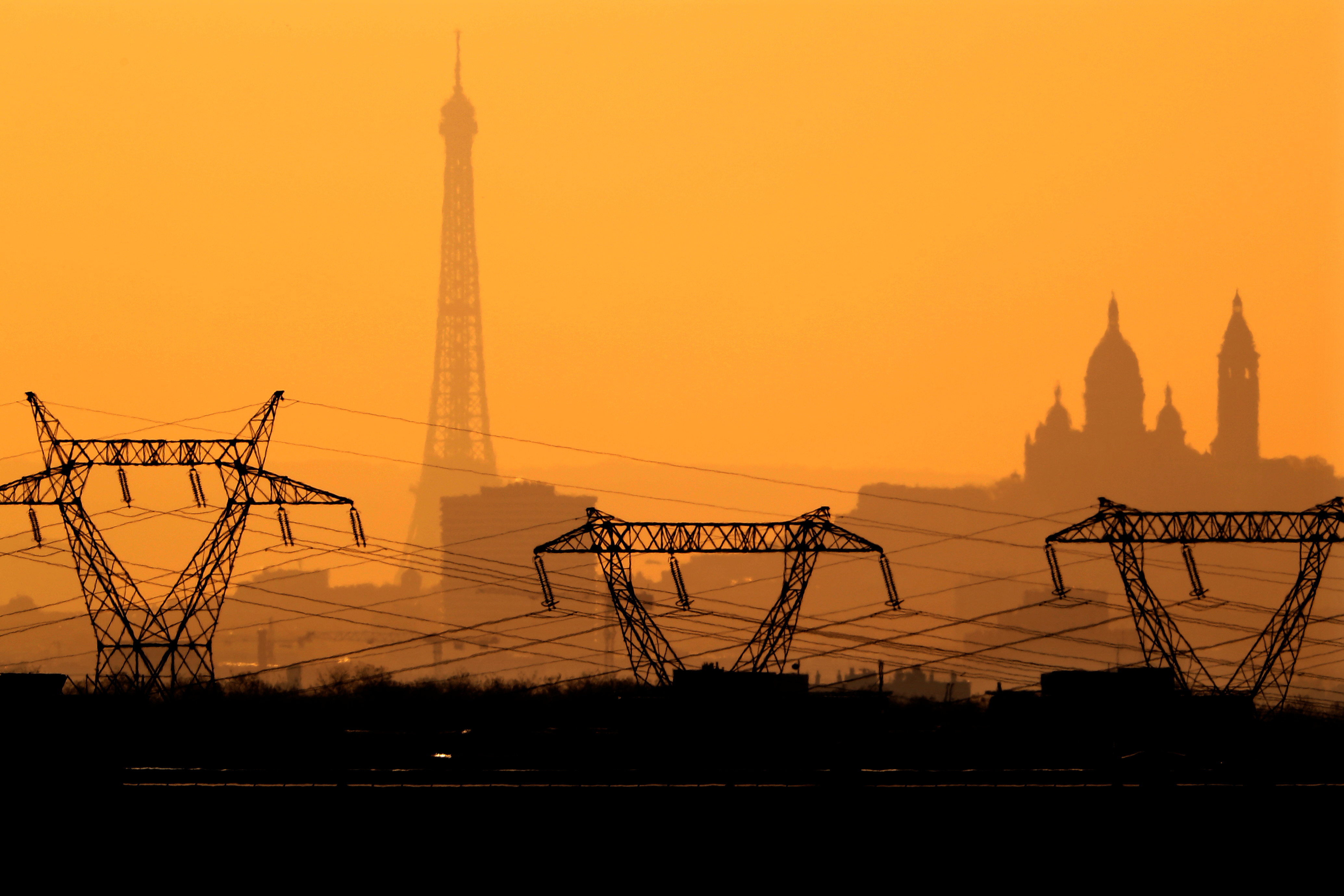 Electricity pylons of high-tension electricity power lines are seen in front of the Eiffel Tower (L) and the Sacre Coeur Basilica on Montmartre from Roissy at sunset