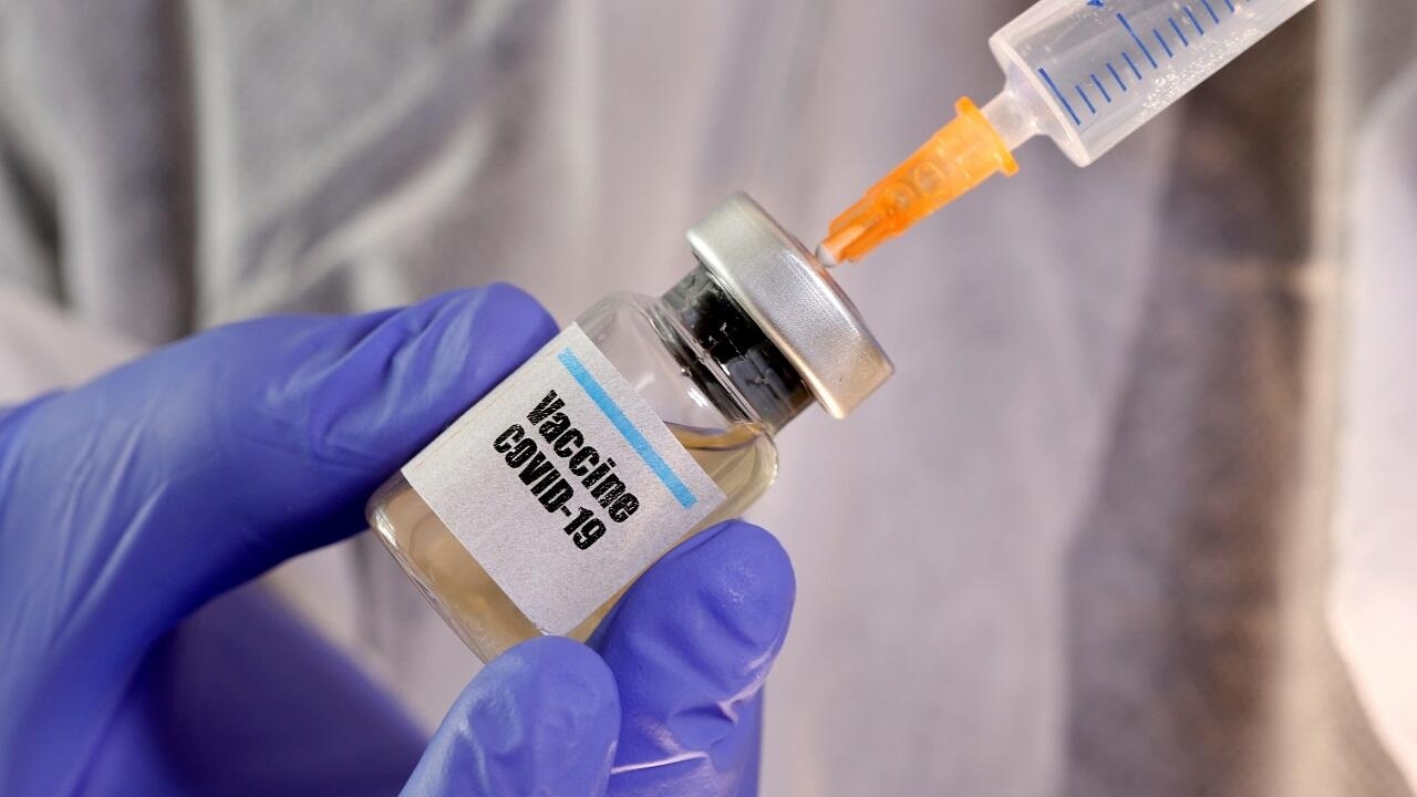 FILE PHOTO: A woman holds a small bottle labeled with a "Vaccine COVID-19" sticker and a medical syringe in this illustration