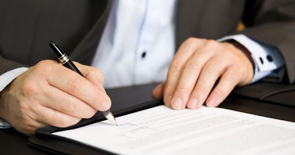 Business person signing a contract, focus on signature.